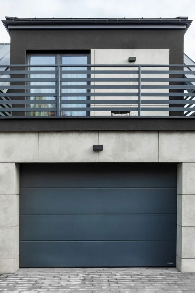 Ciemna brama WIŚNIOWSKI UniTherm w betonowej elewacji pod balkonem