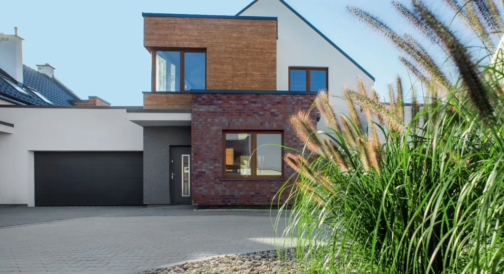 Ciemna brama WIŚNIOWSKI UniTherm przy domu z ceglaną elewacją